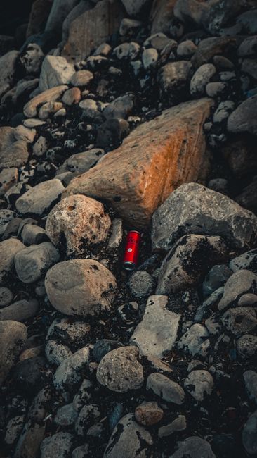 The image depicts the interior of a natural underground tunnel or cave, characterized by rough, textured rock walls with a reddish-brown hue and patches of darker speckled areas. The tunnel is illumin